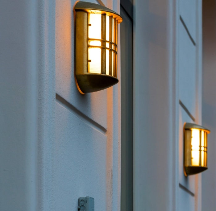 Two golden wall sconces illuminate a textured white building facade. This commercial landscape lighting highlights the clean lines of the architecture, potentially after pressure washing.