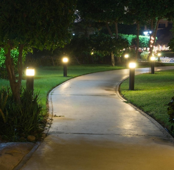 A winding pathway illuminated by landscape lighting at night, with lush green grass and trees on either side. The scene evokes a sense of tranquility and highlights the beauty of commercial landscape lighting.