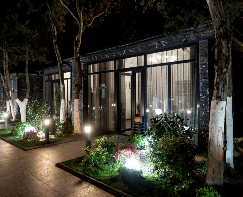 Modern building with commercial landscape lighting at night. Path leads to glass doors, surrounded by illuminated greenery. Pressure washing may be needed to maintain the clean look.