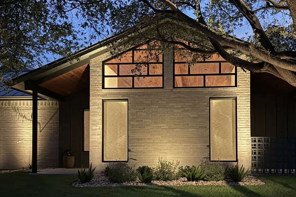 Modern home exterior at dusk, part of The Falcon Project. Light brick facade, geometric windows, and lush landscaping create a welcoming and contemporary aesthetic.