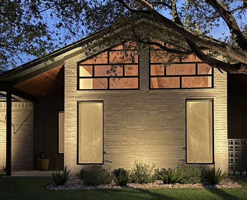 Modern home exterior at dusk, part of The Falcon Project. Light brick facade, geometric windows, and lush landscaping create a welcoming and contemporary aesthetic.