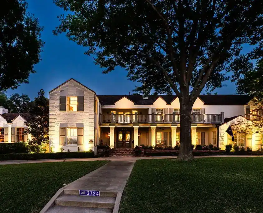 Large two-story colonial-style house lit at dusk, with columned porch, second-floor balcony, front walkway and big tree; curb number 3724.