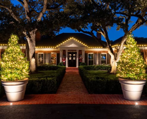 Festive holiday home at Ridgeview, adorned with Christmas lights. Two lit trees flank a brick walkway leading to a red-doored house with garland and lights along the roofline.